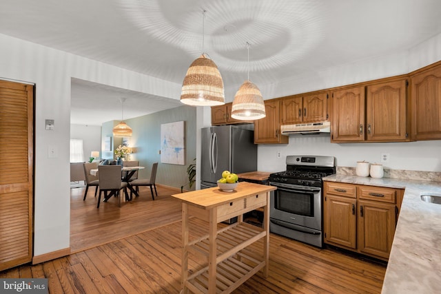 kitchen featuring appliances with stainless steel finishes, under cabinet range hood, light countertops, hardwood / wood-style floors, and hanging light fixtures