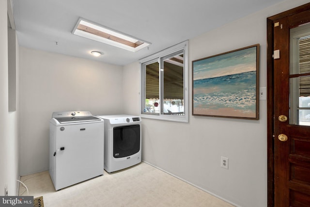 clothes washing area featuring washer and clothes dryer, light floors, and a skylight