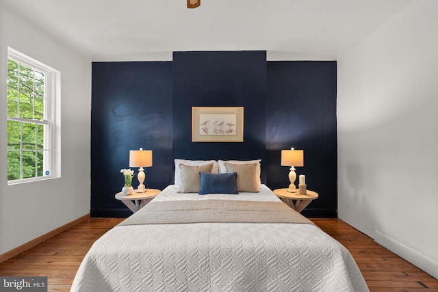 bedroom with multiple windows, wood finished floors, and baseboards
