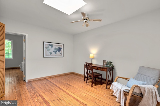 office with a skylight, light wood finished floors, ceiling fan, and baseboards