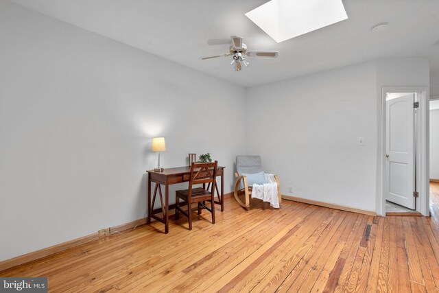 office space featuring a skylight, hardwood / wood-style flooring, baseboards, and a ceiling fan