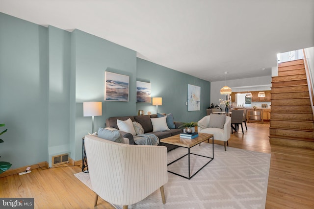 living area featuring stairs, light wood-style floors, and baseboards