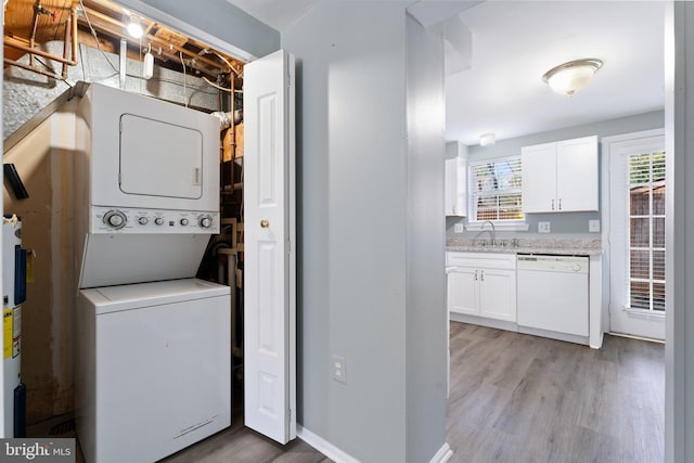 clothes washing area with stacked washer / drying machine, light wood-style flooring, a sink, and laundry area