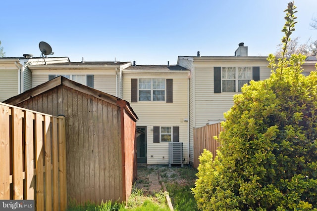 rear view of house with a chimney, fence, and cooling unit