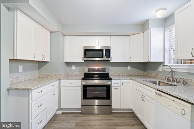 kitchen featuring stainless steel appliances, light wood-style flooring, a sink, and white cabinetry