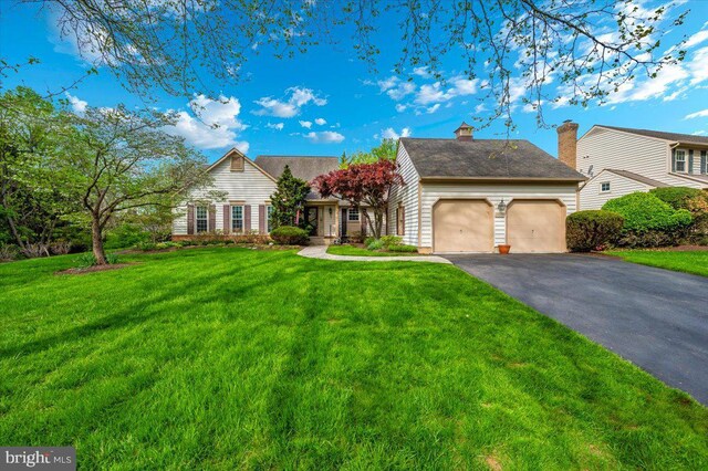 view of front facade featuring driveway, a chimney, a front lawn, and a garage