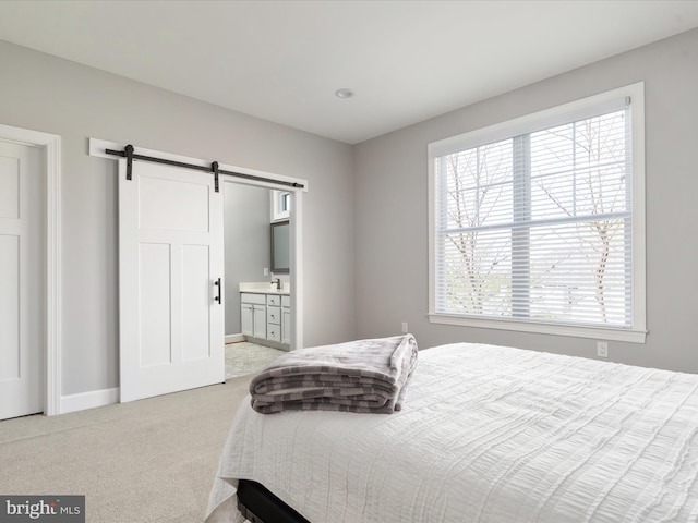 carpeted bedroom featuring ensuite bath, a barn door, baseboards, and multiple windows