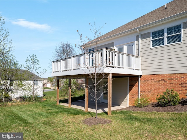 rear view of property with a shingled roof, a wooden deck, a patio, a lawn, and brick siding