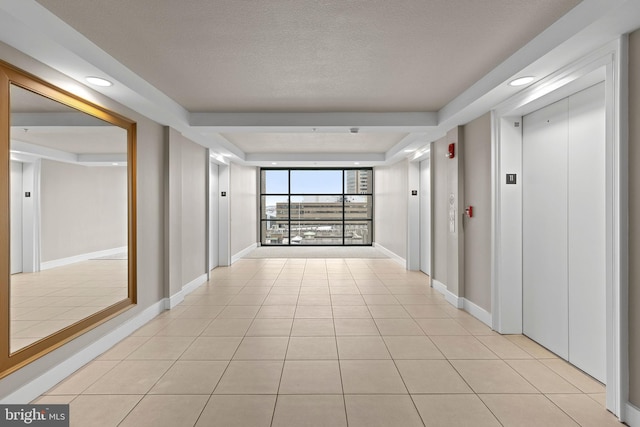 hallway with light tile patterned floors, elevator, and baseboards