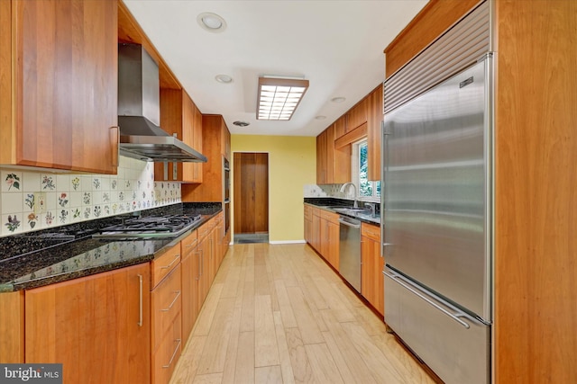 1408 Margarette Ave, Baltimore, MD 21286 - kitchen featuring appliances with stainless steel finishes, wall chimney exhaust hood, decorative backsplash, light wood finished floors, and dark stone countertops