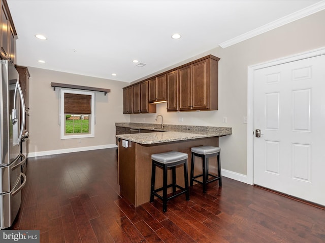 kitchen featuring a peninsula, baseboards, a kitchen bar, stainless steel fridge with ice dispenser, and light stone countertops