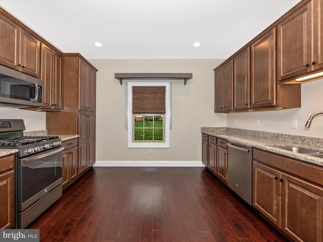 kitchen with stainless steel appliances, dark wood-style floors, a sink, baseboards, and light stone counters