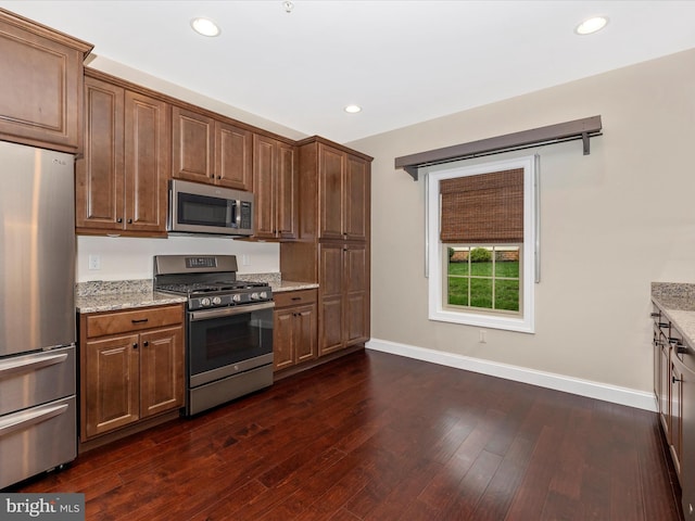 kitchen featuring baseboards, light stone countertops, stainless steel appliances, and dark wood-style floors