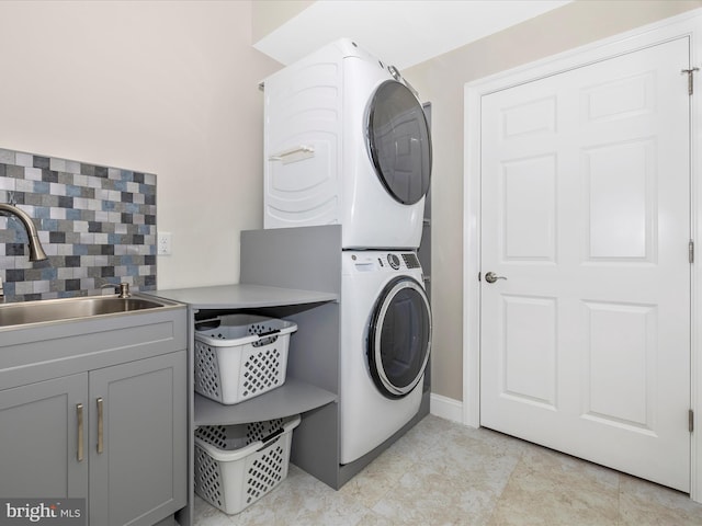 washroom with cabinet space, stacked washer and dryer, and a sink
