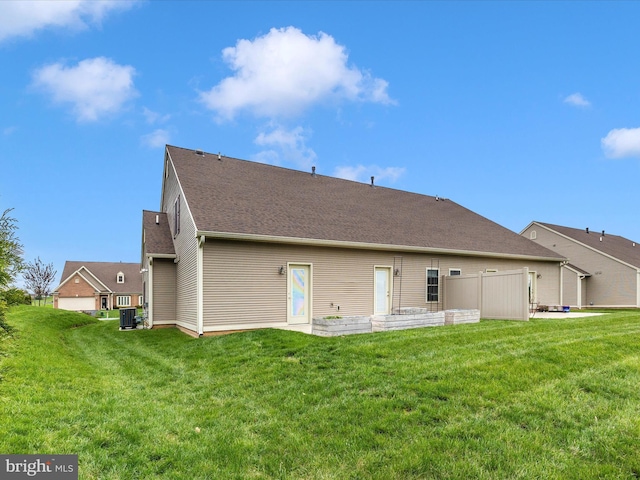 rear view of house featuring a shingled roof, a yard, and central AC