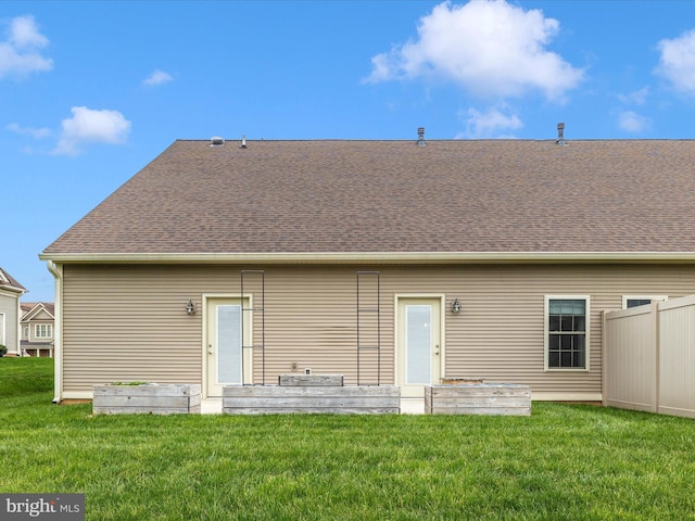 back of property with fence, a lawn, and a shingled roof