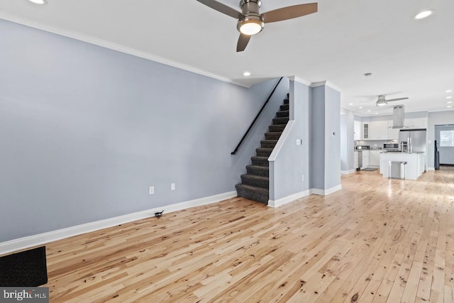 unfurnished living room with crown molding, light wood-style flooring, stairway, baseboards, and a ceiling fan