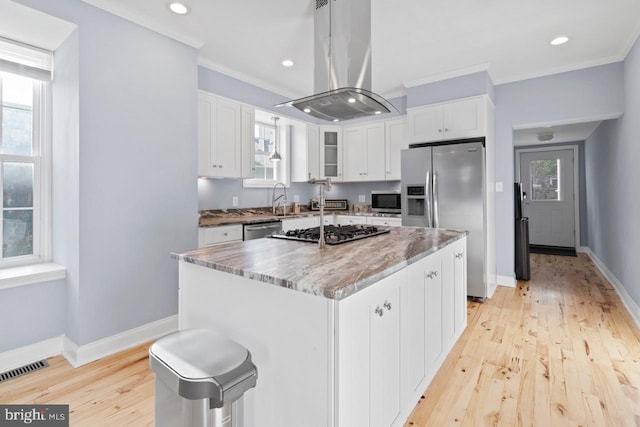 kitchen featuring appliances with stainless steel finishes, white cabinets, island exhaust hood, baseboards, and crown molding