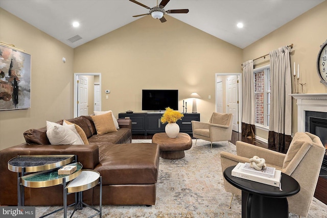 living room with wood finished floors, visible vents, a ceiling fan, a glass covered fireplace, and high vaulted ceiling