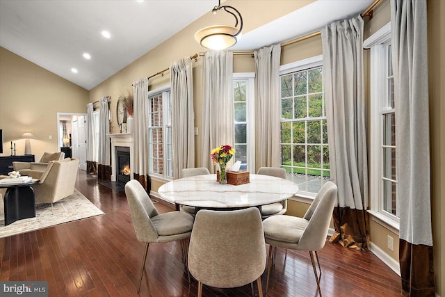 dining space with a glass covered fireplace, baseboards, dark wood finished floors, lofted ceiling, and recessed lighting