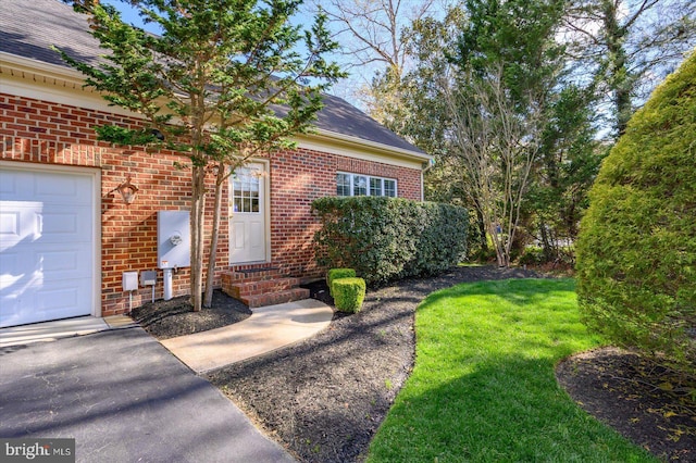 view of exterior entry with brick siding, a yard, and a garage
