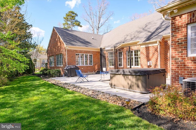 rear view of property with central AC, a patio area, a lawn, brick siding, and a hot tub
