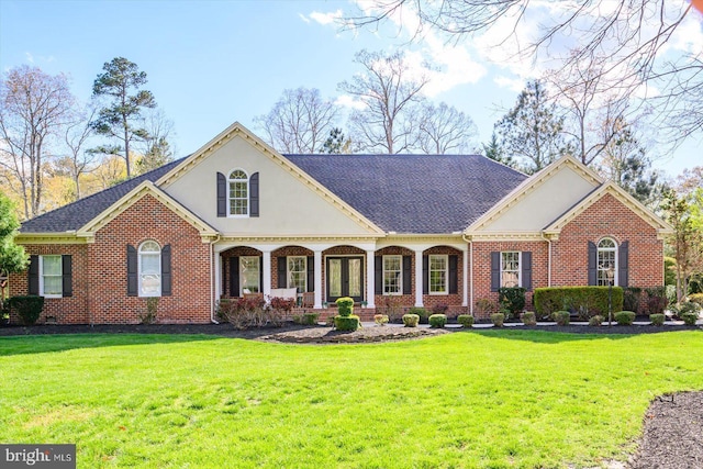 view of front of house with a shingled roof, brick siding, a front yard, and stucco siding