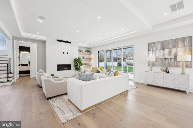living room with visible vents, light wood-style floors, a large fireplace, stairway, and a raised ceiling