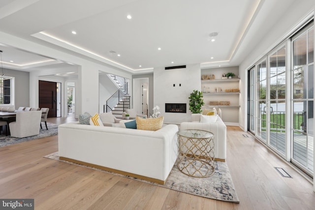 living area featuring light wood finished floors, stairs, and a raised ceiling