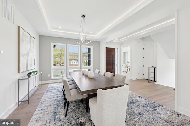 dining room featuring a raised ceiling, baseboards, visible vents, and light wood-type flooring