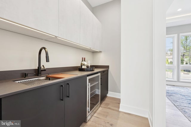 bar with a sink, baseboards, bar, light wood-style floors, and beverage cooler