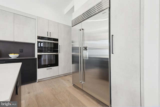 kitchen with double oven, built in refrigerator, modern cabinets, and light wood-style floors