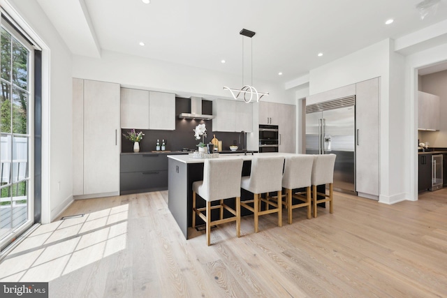 kitchen featuring wall chimney range hood, a center island, modern cabinets, stainless steel appliances, and a kitchen bar