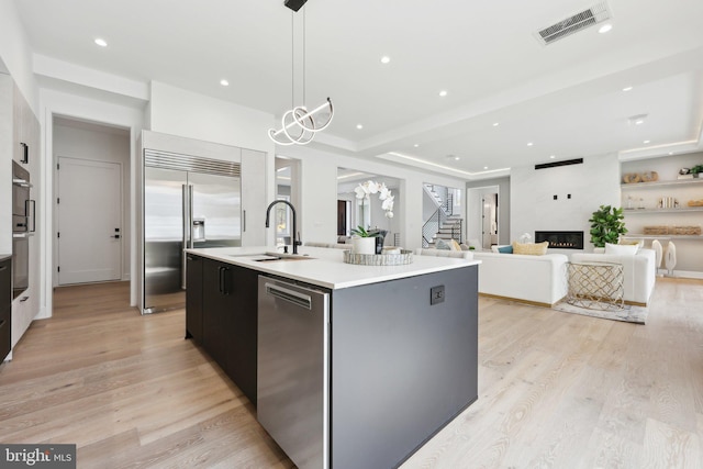 kitchen featuring a sink, a kitchen island with sink, stainless steel appliances, a fireplace, and visible vents