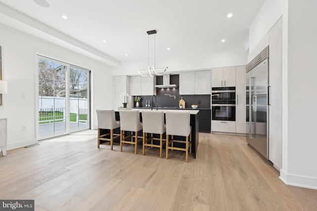 kitchen featuring light wood finished floors, modern cabinets, stainless steel built in fridge, dobule oven black, and a kitchen island with sink