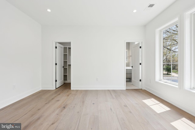 unfurnished bedroom featuring a walk in closet, light wood-style flooring, baseboards, and recessed lighting