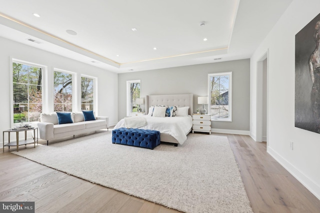 bedroom with wood finished floors, visible vents, a raised ceiling, and multiple windows