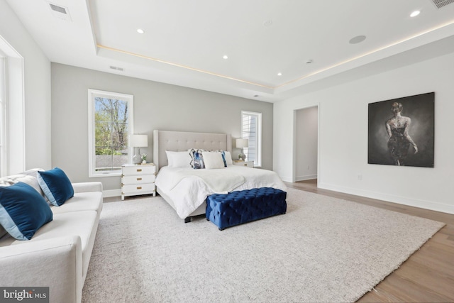 bedroom with visible vents, baseboards, wood finished floors, and a tray ceiling