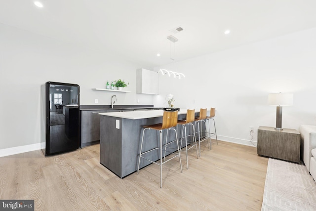kitchen featuring a kitchen breakfast bar, a sink, freestanding refrigerator, light wood-style floors, and baseboards