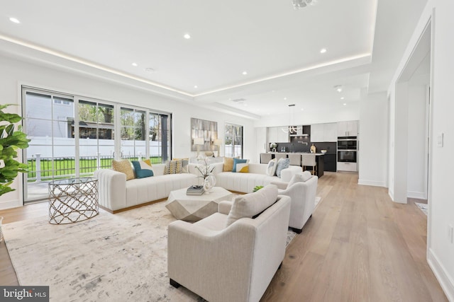 living room featuring a tray ceiling, light wood finished floors, baseboards, and recessed lighting