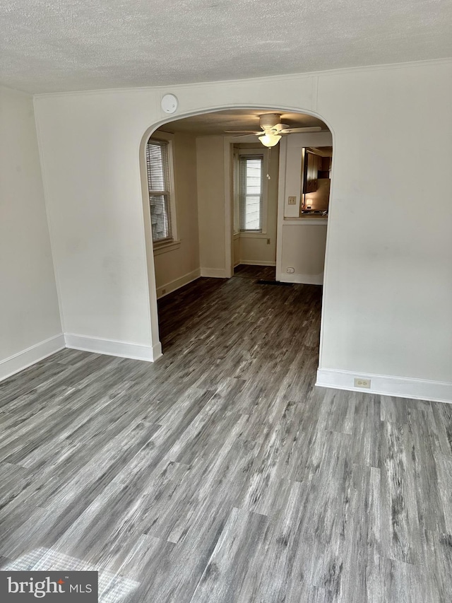 unfurnished room with arched walkways, a textured ceiling, baseboards, and wood finished floors