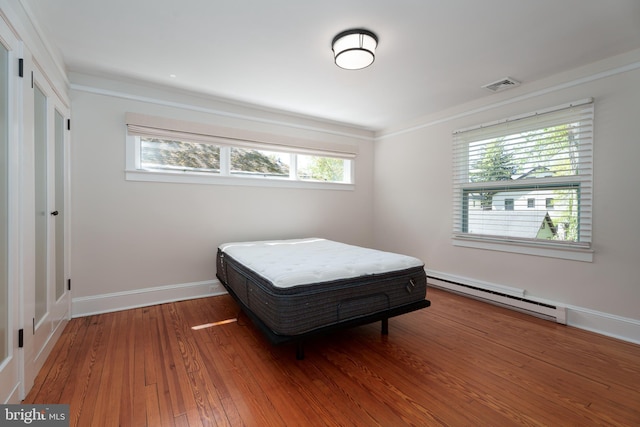 bedroom featuring hardwood / wood-style floors, visible vents, crown molding, baseboard heating, and baseboards