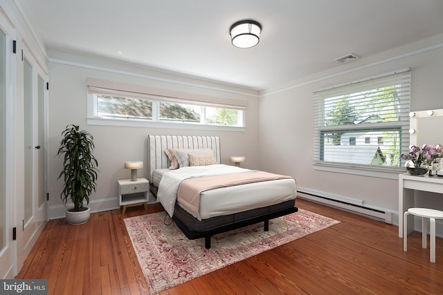 bedroom featuring baseboard heating, baseboards, visible vents, crown molding, and hardwood / wood-style floors