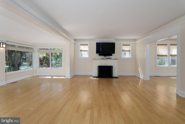unfurnished living room with light wood-type flooring, baseboards, a fireplace with flush hearth, and plenty of natural light