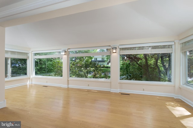 unfurnished sunroom with lofted ceiling, baseboards, visible vents, and wood finished floors