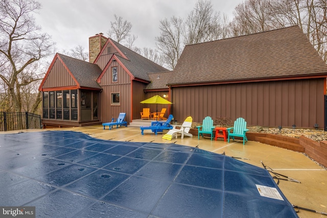rear view of property featuring a patio, a sunroom, a shingled roof, and a chimney