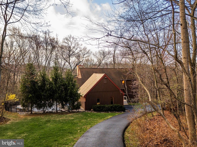 view of front facade with fence, a chimney, a front yard, roof with shingles, and driveway