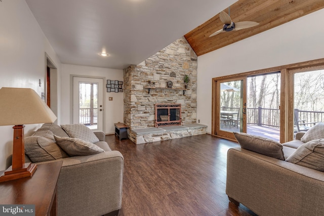living room featuring high vaulted ceiling, wooden ceiling, a ceiling fan, a stone fireplace, and dark wood-type flooring