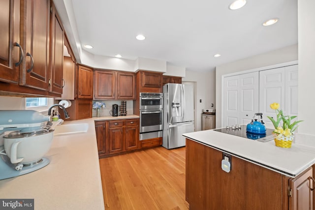 kitchen featuring light countertops, a sink, light wood finished floors, a warming drawer, and stainless steel appliances