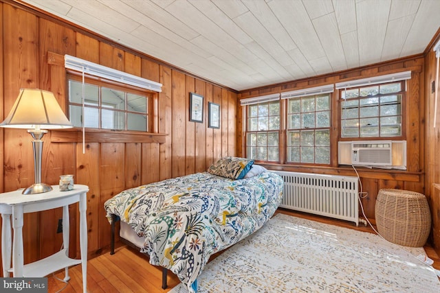 bedroom featuring wood-type flooring, radiator heating unit, cooling unit, and wood walls